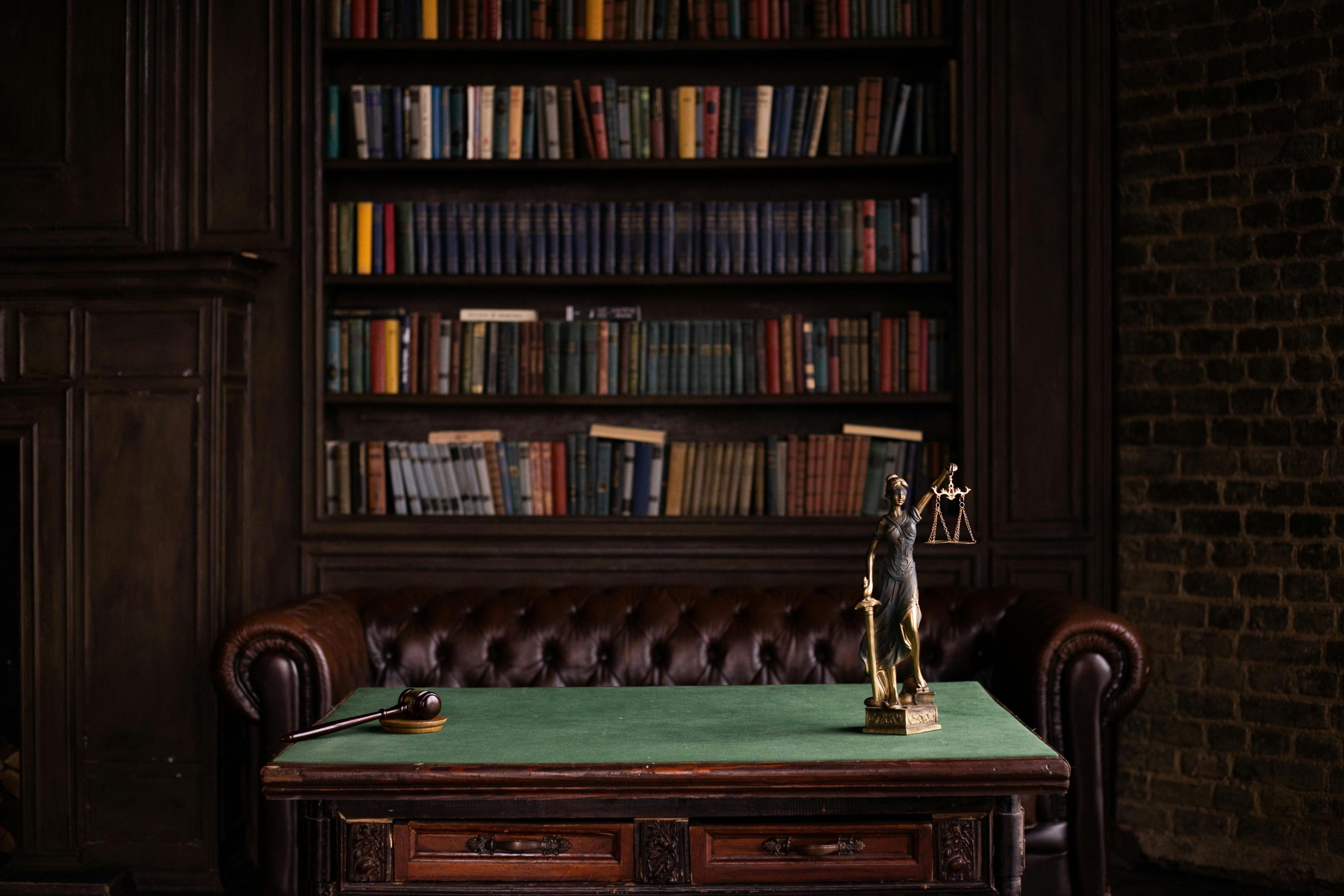 services-02 A classic study room with shelves of books, a gavel, and Lady Justice figurine on a green table.